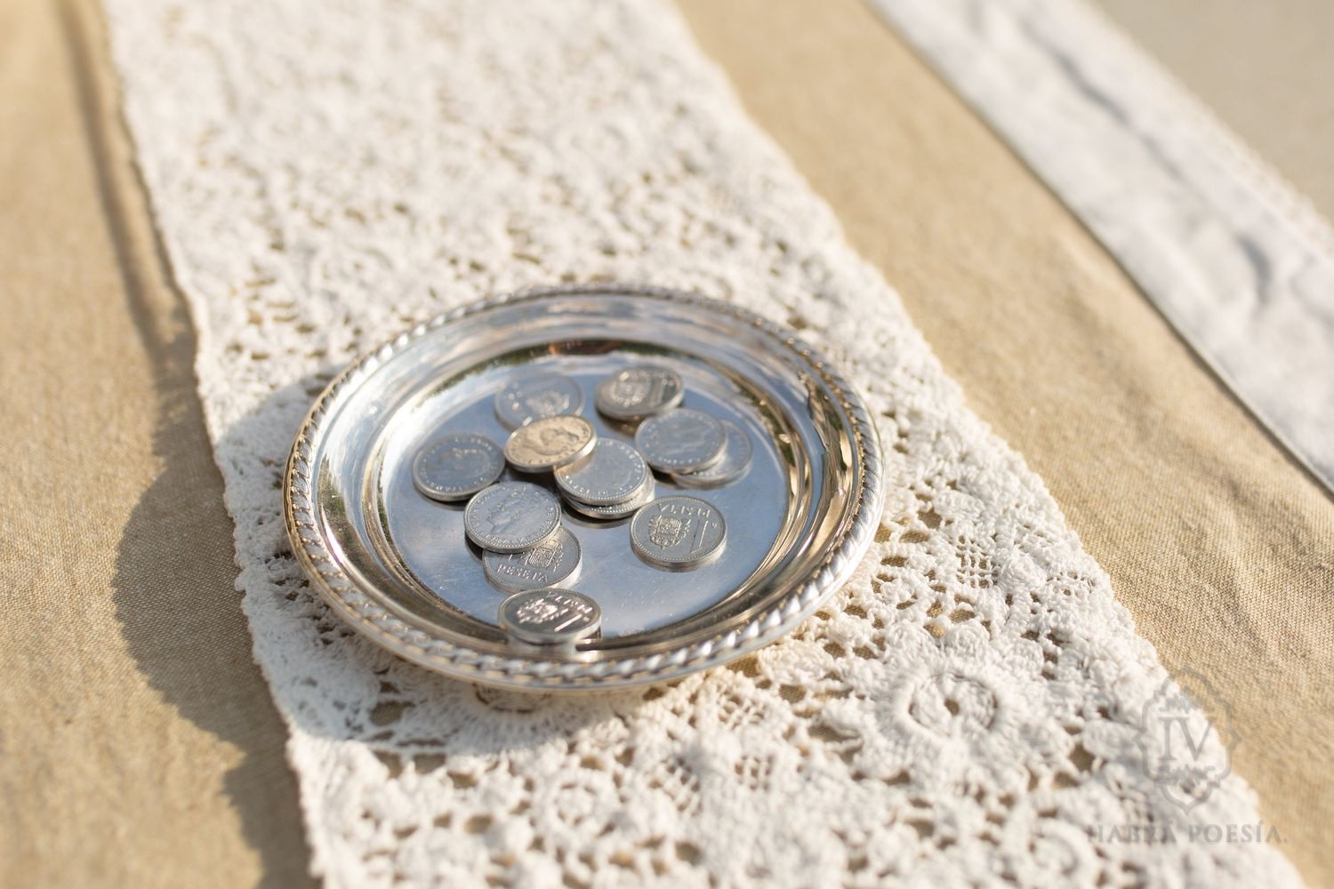 Arras de boda: monedas en una bandeja de plata sobre encaje