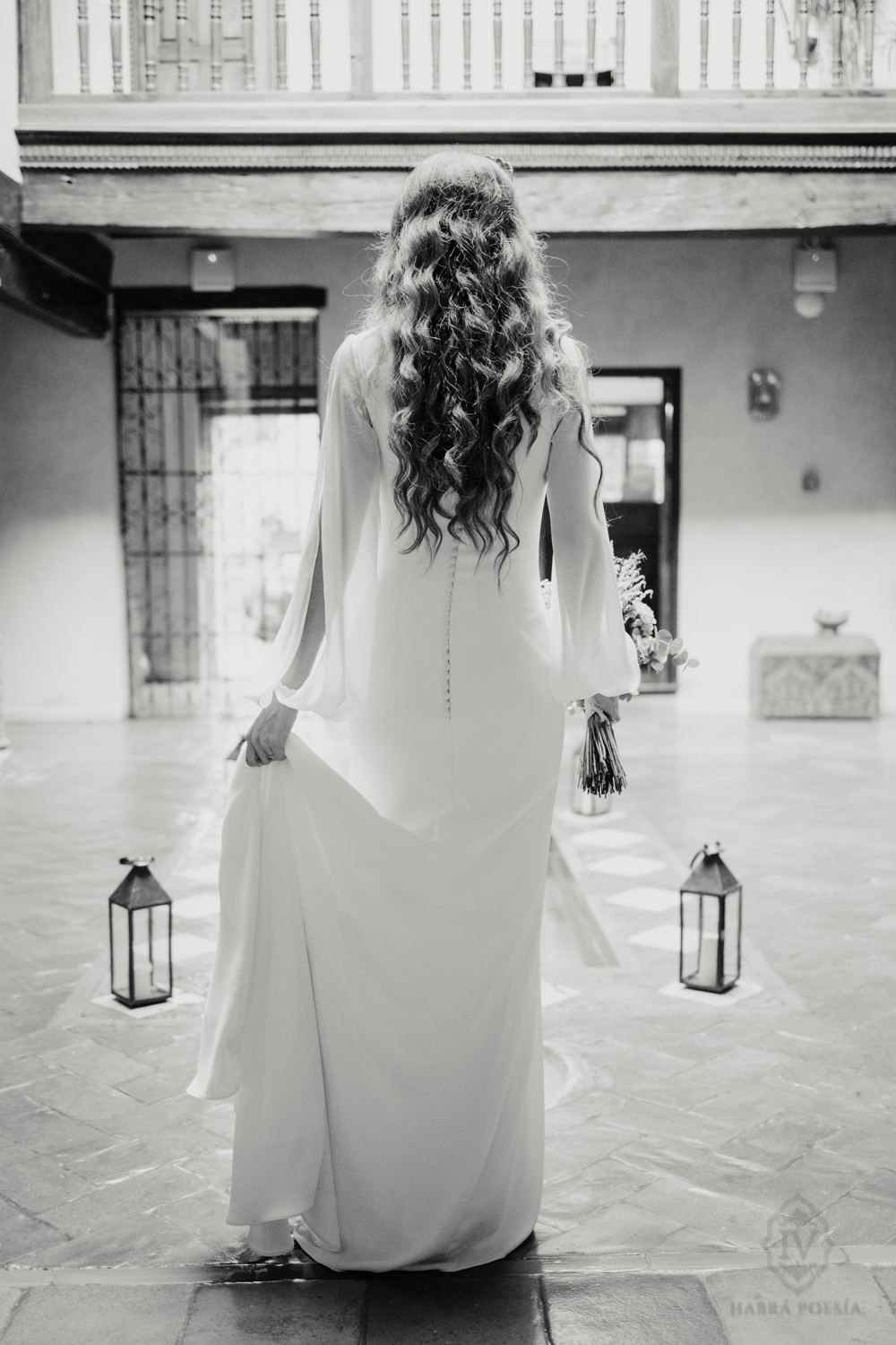 Novia de espaldas en un patio con farolillos, en blanco y negro